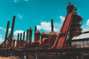 Rostige Industrieanlage mit Schloten und Förderturm unter blauem Himmel