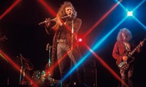 Progressive-Rock-Band mit Flötist und Gitarrist auf einer farbig beleuchteten Bühne